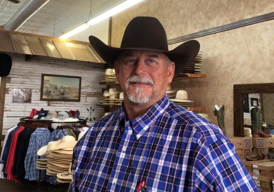 A man in a cowboy hat standing next to shelves.